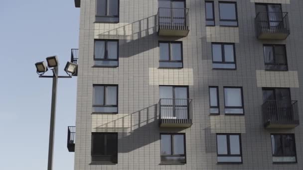 Onderaanzicht van residentiële nieuwbouw gemaakt van witte bakstenen. Actie. Fragment van een witte baksteen nieuw appartement huis met balkons en straatlantaarns tegen een heldere hemel. — Stockvideo