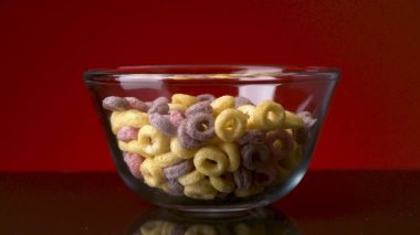 Yemek ve kahvaltı kavramı. Stok görüntüleri. Renkli halka mısır gevreklerinin yakın plan koyu masa yüzeyinde şeffaf cam bir kase ve kırmızı duvar arka plan. 