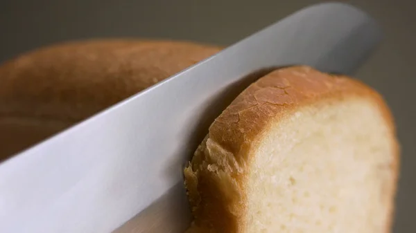 Gri arka planda izole edilmiş ekmek kesmek. Stok görüntüleri. Yakın plan, taze pişmiş bir somun ekmeği keskin çelik bir bıçakla kesmek, yiyecek kavramı.. — Stok fotoğraf