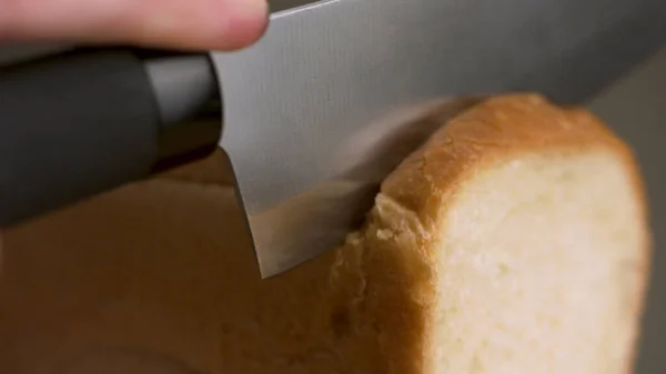 Brood gesneden geïsoleerd op grijze achtergrond. Voorraadbeelden. Close up van de hand snijden van een vers gebakken brood van wit brood met een scherp stalen mes, voedsel concept. — Stockfoto