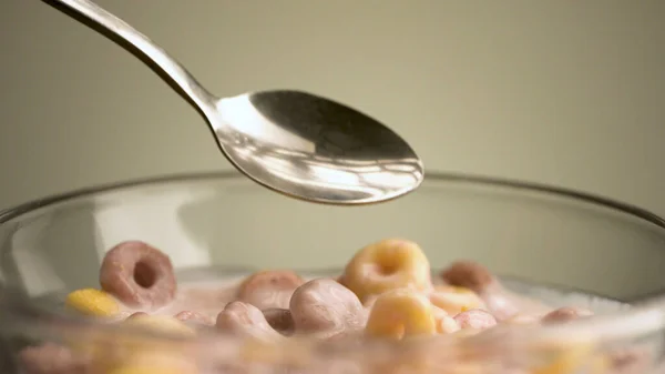 Concepto de desayuno y comida. Imágenes de archivo. Primer plano de comer coloridos anillos de maíz deliciosos y dulces y yogur de frutas con una cuchara en un tazón transparente de vidrio aislado sobre un fondo beige. —  Fotos de Stock