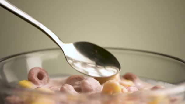 Concepto de desayuno y comida. Imágenes de archivo. Primer plano de comer coloridos anillos de maíz deliciosos y dulces y yogur de frutas con una cuchara en un tazón transparente de vidrio aislado sobre un fondo beige. — Vídeo de stock