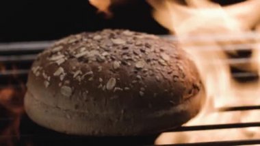 Taze pişmiş yuvarlak ekmeği ızgarada ateşte pişirin. Stok görüntüleri. Mısır gevrekli ve tohumlu lezzetli ekmek. Siyah zemin üzerinde ateş alevi ile izole edilmiş.. 