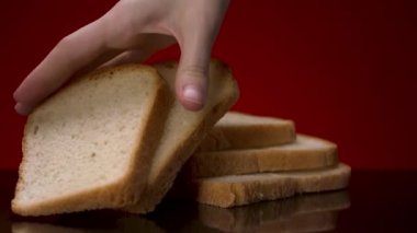 Dilimlenmiş taze ekmek siyah masada yatıyor. Stok görüntüleri. Kırmızı zemin üzerinde izole bir şekilde duran fırınlanmış beyaz ekmek dilimlerinden birini ele alalım..