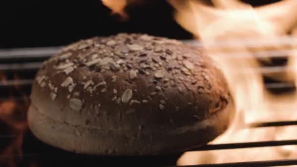 Close up of freshly baked round shaped loaf of bread on grill with fire. Stock footage. Tasty bread with cereals and seeds isolated on black background with fire flame. — Stock Video