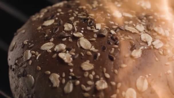 Freshly baked round bread rotating against black background. Stock footage. Close up tasty pastry product for the breakfast , loaf with sunflower seeds and oat flakes. — Stock Video