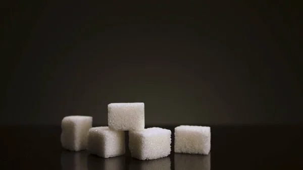 Pyramid of white sugar cubes isolated on dark background. Stock footage. Close up of white pieces of sugar, concept of diabetes and obesity.