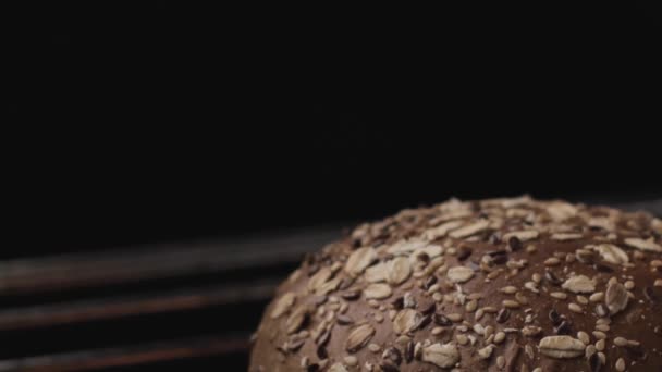 Close-up van vers gebakken rond brood op grill met vuur. Voorraadbeelden. Lekker brood met granen en zaden geïsoleerd op zwarte achtergrond met vuur vlam. — Stockvideo