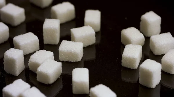 Şeker küplerinin yarısını masadan fırçalamak, şeker ve şeker yemekten vazgeçmek. Stok görüntüleri. Siyah arkaplanda izole edilmiş beyaz şeker parçaları. — Stok fotoğraf