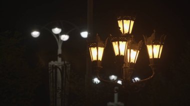 Siyah gökyüzü arka planında iki farklı sokak feneri. Stok görüntüleri. Eski moda ve modern sokak lambaları. Geceleri şehir sokaklarında sarı ve beyaz ışıklar..