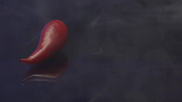 Fresh red chilly pepper with smoke isolated on a black background. Stock footage. Concept of spicy and hot vegetarian food, close up of red pepper covered by white smoke.