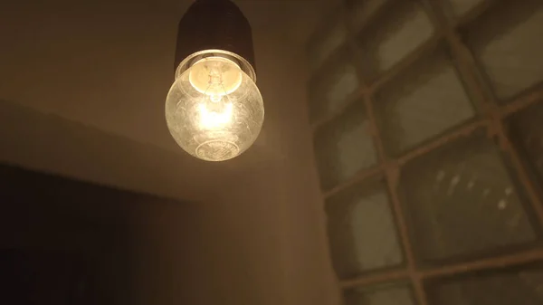 Vista inferior de uma lâmpada pendurada balançando dentro da entrada de uma buiulding. Imagens de stock. Close-up de uma lâmpada de luz amarela piscando em uma atmosfera escura e mística de um edifício. — Fotografia de Stock