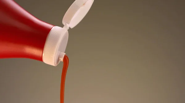 Close up of ketchup pouring from a bottle isolated on a beige background. Stock footage. Concept of cooking food, close up of red bottle of ketchup with white lid. — Stock Photo, Image