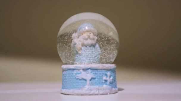 Рождественский волшебный шар с Дедом Морозом. Концепция. Крупный план новогоднего символа - стеклянный шар с падающим снегом внутри, сувенир, стоящий на поверхности белого стола. — стоковое видео