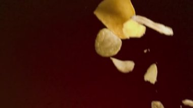 Patates cipsi yavaş çekimde düşüyor. Stok görüntüleri. Kırmızı arka planda izole edilmiş, çıtır çıtır lezzetli cipslere yakın, abur cubur konsepti..