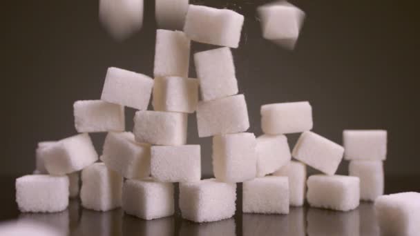 Kostki cukru na odosobnionym tle. Materiał filmowy. Wieża kostek cukru zapada się na odosobnionym tle. Słodycze w dużych ilościach są szkodliwe dla zdrowia. Cukier i słodycze są uzależnieniem XXI wieku. — Wideo stockowe