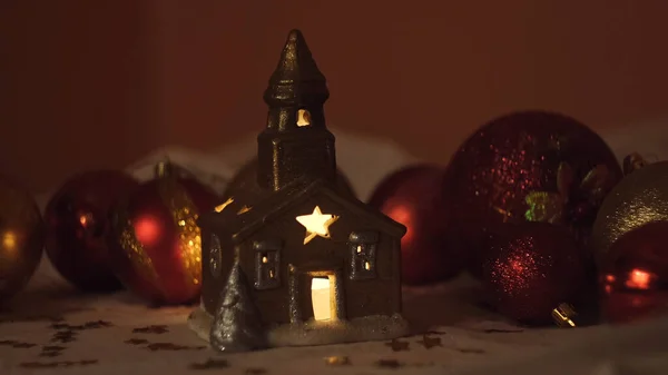 Красивый маленький домик со свечой внутри. Концепция. Закрыть красивый свет свечи внутри маленькой церковной игрушки на фоне красных елочных шаров. — стоковое фото