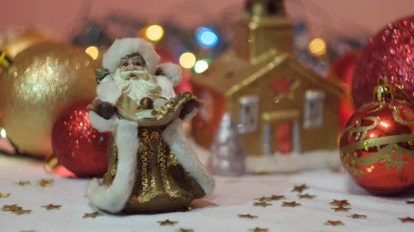 Miniaturspielzeug traditioneller Weihnachtsmann vor leuchtenden Girlanden und Weihnachtsbaumspielzeug. Konzept. Nahaufnahme von Silvester-Souvenirs und Spielzeug. — Stockfoto