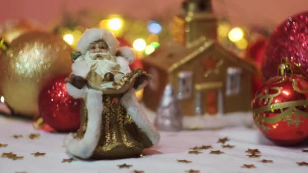 Миниатюрные игрушки традиционного Деда Мороза перед сверкающими гирляндами и игрушками с ёлками. Концепция. Закрытие новогодних сувениров и игрушек. — стоковое видео