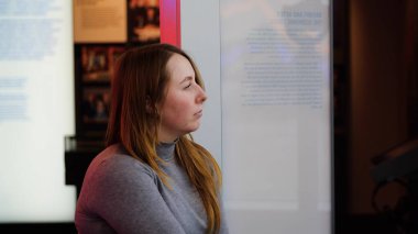 Genç bir kadın binada bekliyor. Medya. Güzel bir kadın, müzedeki reklam standında bekleyen birini bekliyor. Genç kadın turnede müzede sıkılıyor.