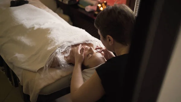 Profesionální masér dává masáž obličeje ženě. Akce. Profesionální masáž obličeje v lázních. Příjemná a omlazující masáž obličeje — Stock fotografie