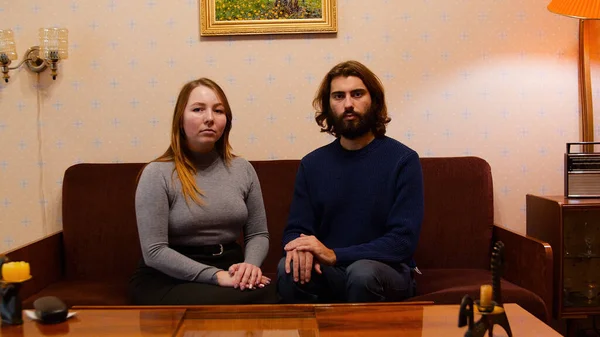 Young couple sitting on old sofa. Media. Young couple posing sitting in old living room. Old interior of my grandmothers apartment. Old Russian 90s interior