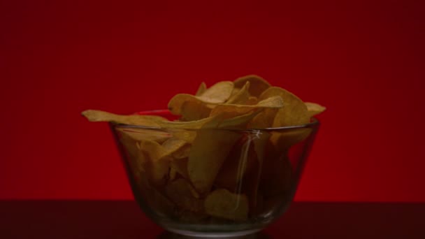 Крупный план ручного сбора чипсов. Запись. Человек берет один картофельный чип из миски на изолированном фоне. Чипсы в прозрачной миске на красном фоне. Еда и закуски — стоковое видео