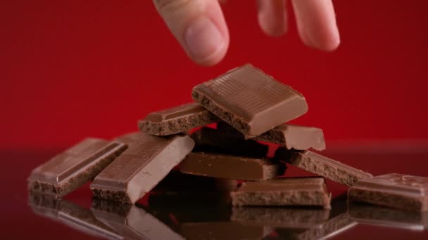 Een hoop chocoladestukjes. Voorraadbeelden. Close-up van de hand nemen stuk chocolade uit stapel op geïsoleerde achtergrond. Stapel chocoladerepen. Heerlijke chocoladerepen. Zoetekauw — Stockvideo