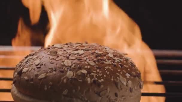 Bun pe fundalul focului. Înregistrări stoc. Pâinea din cereale pentru hamburgeri este la grătar cu foc. Loaf este gătită pe foc la grătar. Gătit Burger pe grătar. Iadul de friptură pe grătar — Videoclip de stoc