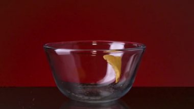 Küçük bir cam kaseye yakın ve içine ve karanlık masaya bir sürü patates cipsi düşüyor. Stok görüntüleri. Kırmızı duvar arka planında baharatlı lezzetli cipsler, abur cubur yeme kavramı.. 