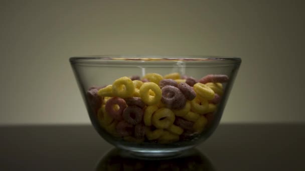 Colazione sana con anelli di cereali colorati. Filmati delle scorte. Primo piano di ciotola di vetro trasparente con deliziosi anelli di mais dolce serviti su tavolo scuro. — Video Stock