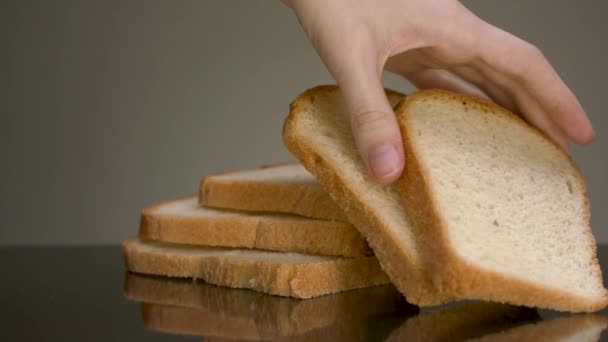 Close up of tasty baked bread slices with crispy crust lying on reflective surface isolated on grey background. Stock footage. Male hand taking slowly a piece of cut white bread loaf. — Stock Video