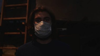 Ahşap merdivenin önünde koruyucu maske takan genç bir adamın portresi ve filmli bir ekran. Medya. Önleme kavramı Covid 19 salgını ve iş yerinde maske takmak.