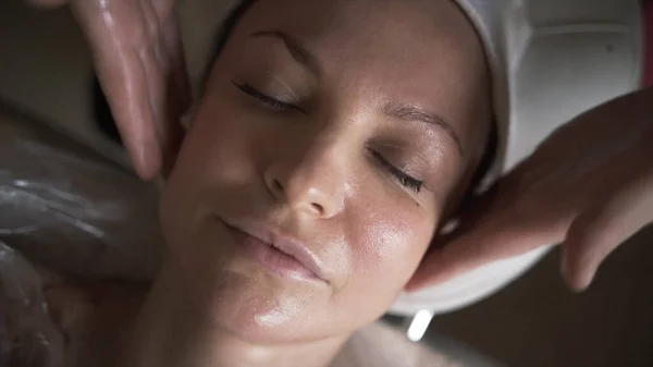 Schöne junge Frau entspannt sich mit Gesichtsmassage im luxuriösen Wellness-Salon, aus nächster Nähe. Handeln. Draufsicht der Hände des Kosmetologen bei der manuellen Massage. — Stockfoto