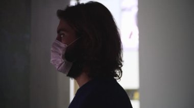 Sinemada dijital ekranın önünde duran tıbbi maske takan bir gencin yan görüntüsü. Medya. Covid 19 salgını sırasında eğlence kavramı. 