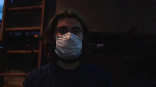 Portrait d'un jeune homme portant un masque médical de protection devant une échelle en bois et l'écran avec film. Les médias. Concept de prévention Covid 19 pandémie et port de masques au travail. — Video