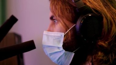 Radyoyu, DJ 'i ya da spor programı yorumcusunu kapat. Medya. 19 numaralı salgın sırasında iş yerinde kulaklık takan ve maske takan genç bir adamın yan görüntüsü..