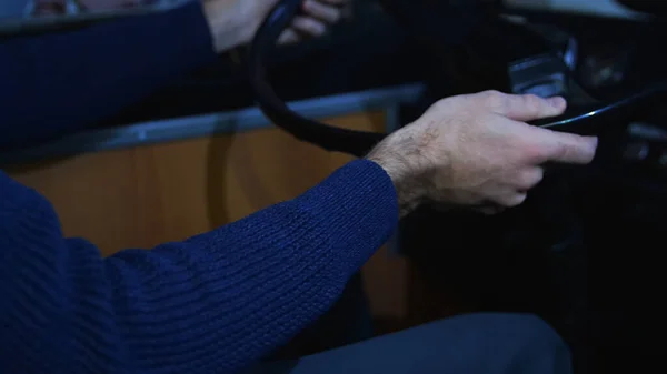 El conductor pone las manos en el volante de un autobús. Medios. Primer plano de un conductor masculino con suéter de punto azul conduciendo un autobús tarde en la noche bajo la luz de la linterna de la calle. — Foto de Stock