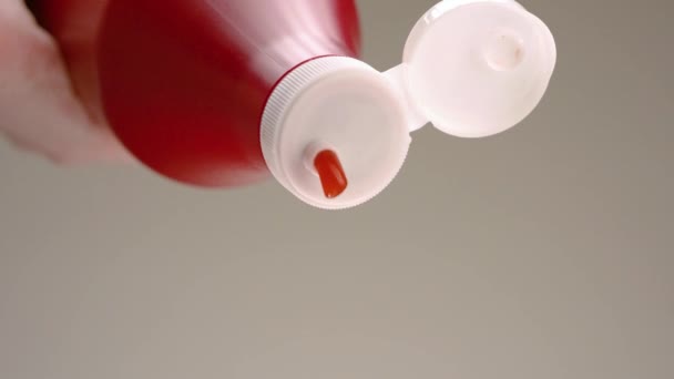 Ketchup being squeezed out of bottle. Stock footage. Close-up of jet of red ketchup on gray background. Ketchup spills out of large red bottle — Stock Video