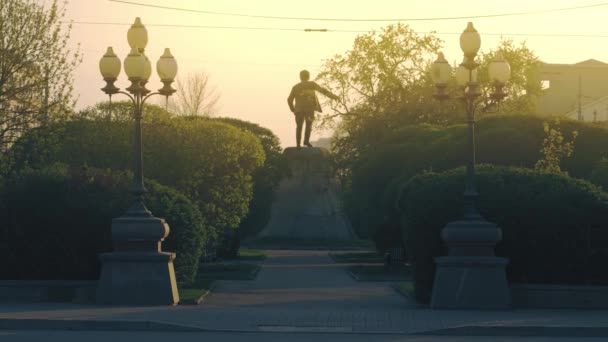 Hermoso callejón verde y arbustos en la calle de la ciudad. Imágenes de archivo. Vista trasera de un monumento rodeado de vegetación de verano sobre el fondo dorado del sol caliente. — Vídeo de stock