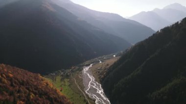 Dağ zirvelerinin havadan görünüşü ve güneşli bir yaz gününde akan bir akarsu bulutlu bir gökyüzünde. Başla. Dağlarda ve ormanlık tepelerde güzel yollar.