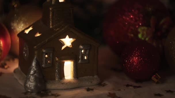 Vela encendida en una casa de candelabro de oro de pie sobre tela blanca como la nieve sobre el fondo colorido de los juguetes de pelota. Concepto. Año nuevo y Navidad y días festivos. — Vídeo de stock