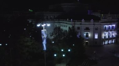 Modern gece şehrinde fenerlerle aydınlatılmış eski bir bina. Stok görüntüleri. Geceleri modern şehrin merkezindeki aydınlık eski binanın üst manzarası. Yaz gecelerinde şehrin eski binasında güzel fenerler