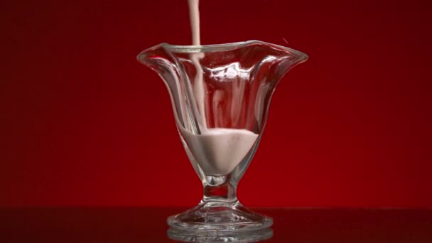 Close-up van yoghurt in glazen beker op rode achtergrond. Voorraadbeelden. Verse yoghurt wordt in helder glas gegoten. Stroom van smoothies vult glas op geïsoleerde achtergrond — Stockvideo