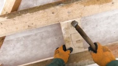 Adam çatıdaki tahta çerçeveye çivi çakıyor. Şarjör. Marangozluk, ahşap evin çatısında çalışıyor. İnsan kışın ev için ahşap yapı inşa eder. Birinci şahıs vuruldu.