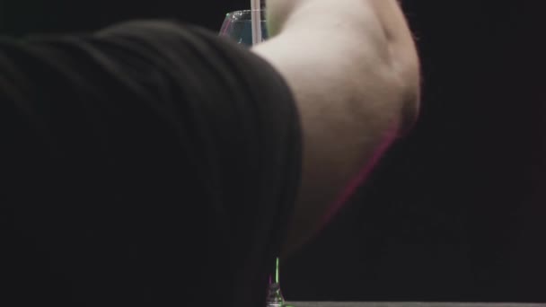 Приблизний бармен з блакитним напоєм. Відеоматеріал. Бармен ворушить алкогольним напоєм у прозорому склі. Синій напій починає світитися і мерехтіти, коли його перемішують. — стокове відео