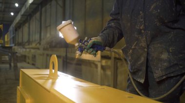 İşçi sprey tabancayla kiriş boyuyor. Şarjör. Fabrikada boyacı sprey boya metal parçası. İşçi fabrikadaki parlak fenerin arka planına çelik kiriş çiziyor.