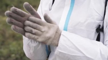 Koruyucu beyaz takım elbiseli, pamuklu eldivenli, işe hazırlanan bir adam. Başla. Yeşil çimen arka planında beyaz kumaş eldivenli erkek ellerini kapat..