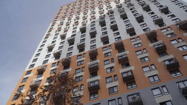 Yeni konut binasının önündeki bir sonbahar çalısı ve gökyüzü manzarası. Başla. Kırmızı yapraklı bir ağaç ve yüksek katlı bir ev.