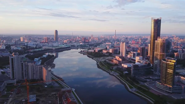 Prachtig panorama van de moderne stad met reflectie van de lucht in de rivier bij zonsondergang. Voorraadbeelden. Moderne stad werd roze geschilderd door ondergaande zon. Hoogbouw reflecteert ondergaande zon op de achtergrond van roze stad — Stockfoto